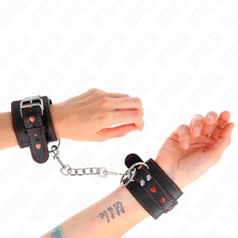 KINK - SCHWARZE HANDGELENKFESSELN MIT ROTER HERZEINLAGE, VERSTELLBAR 21-28 CM X 5,5 CM - Vanelion Paradise